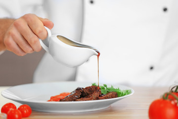 Chef pouring sauce on meat dish on table