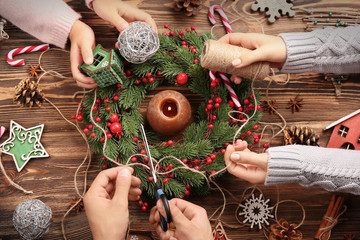 Family decorating Christmas wreath  on wooden background
