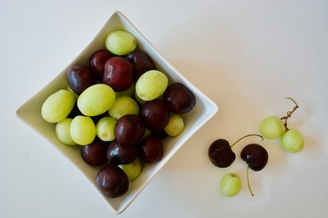Tasty cherries and grapes in the white square plate on the white table 