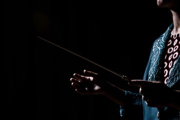 The hands of a female orchestra conductor directing the musicians in the darkness. Side shot.
