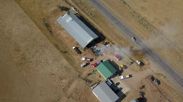 Aerial circle around rural farm barn fire smoke 4K. Farming and ranch facility with storage barns and buildings. Fire department respond to spontaneous fire inside hay bales and feed.