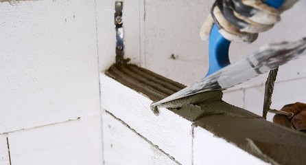 Building worker use a trowel for levelling a mortar bed on autoclaved aerated concrete blocks wall.