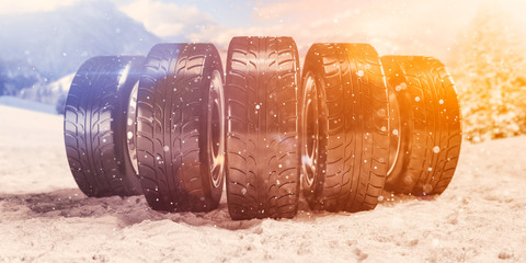 Eine Gruppe Winterreifen auf verschneiter Fahrbahn vor winterlicher Kulisse 