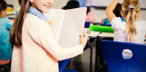 Portrait of schoolgirl standing with book in classroom