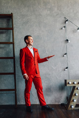 Studio portrait of a happy modern man in a white shirt and red suit against a gray background.