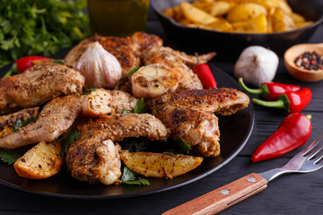 Grilled chicken wings, baked potatoes, herbs and spices on kitchen table. Hot fresh appetizing countryside food. Cooking concept, meat dishes, homemade cuisine