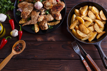 Grilled chicken wings, baked potatoes in a pan, cutlery, herbs and spices on kitchen table. Kitchen background, cooking concept, free space for advertisement or text