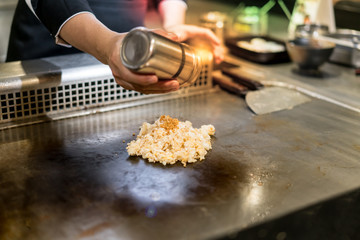 Hand of Chef cooking garlic fried rice on hot pan in front of customers.