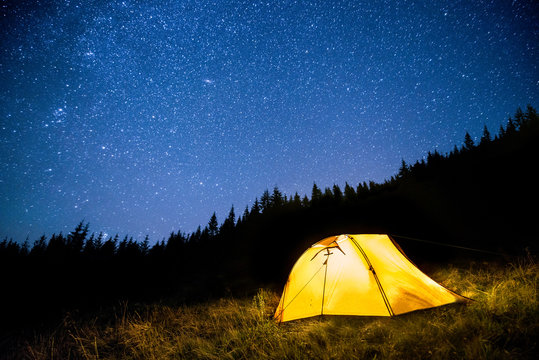 Glowing camping tent in the mountain forest under a starry sky