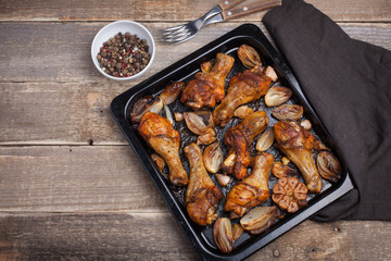 Oven baked chicken legs with onions, garlic and a mixture of peppers on dark wooden background closeup. Top view with copy space