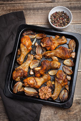 Oven baked chicken legs with onions, garlic and a mixture of peppers on dark wooden background closeup. Top view