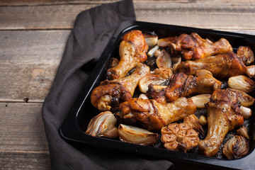 Oven-baked chicken leg quarters with onion, garlic and capsicum on a dark background closeup. Top view