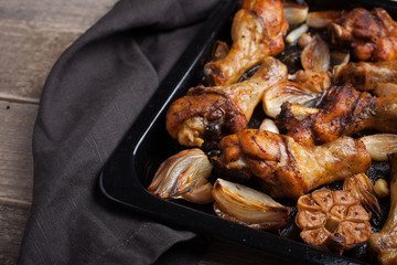 Oven-baked chicken leg quarters with onion, garlic and capsicum on a dark background closeup. Top view