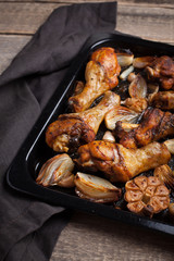 Oven-baked chicken leg quarters with onion, garlic and capsicum on a dark background closeup. Top view