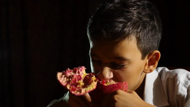 little hungry boy a vegetarian eating a pomegranate with greed at night. 4k, slow-motion.