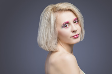 Beauty and fashion Ideas. Portrait of Caucasian Blond Female With Vivid Artistic Facial Makeup Against Gray.