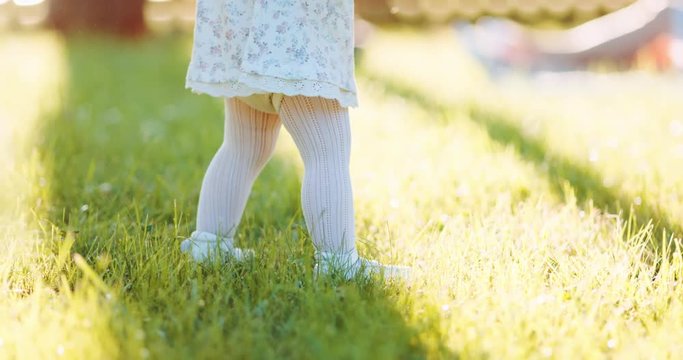Little baby learns to walk. First Steps. Slow Motion 120 fps, 4K. Toddler Girl Walking on a green grass in summer. Close up on feet. Happy childhood concept. Family time.