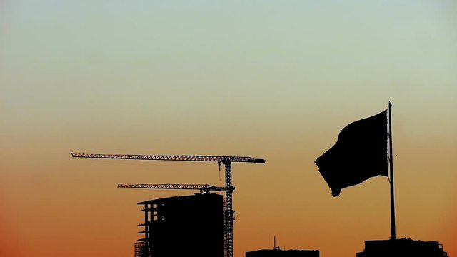 silhouette Turkish flag slow motion waving front of Turkish economy&rsquo;s dynamo construction building at sunset