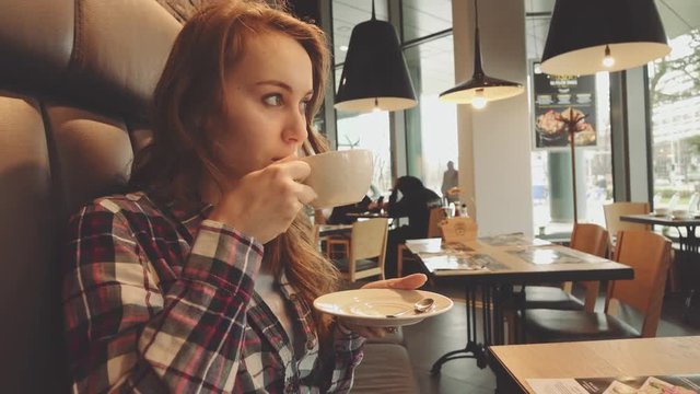 Woman drinking coffee in a cafe, 4K Slow Motion 120 fps. Stabilazed dolly shot. Young beautiful calm woman enjoying a cup of hot coffee in the restaurant. Relaxed morning breakfast in a city. 