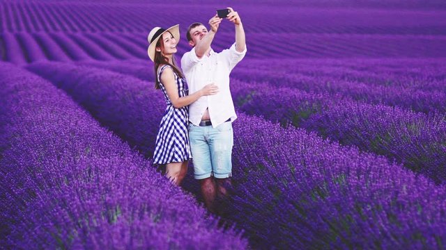 Young Couple Taking Selfie on Smart Phone in Endless Lavender Fields. SLOW MOTION 120 FPS. Handsome Man and Beautiful Woman tourists in blooming lavender field. Plateau du Valensole, South France.