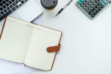 Modern White office desk table with pen, leather notebook,calculator,laptop and cup of coffee.Top view with copy space.Working desk table concept.