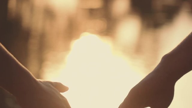 Close Up Of Two Lovers Joining Hands. SLOW MOTION 240 Fps. Detail Silhouette Of Man And Woman Holding Hands Over The Sunset Lake Background. Couple Trust, Love And Happiness Concept. 