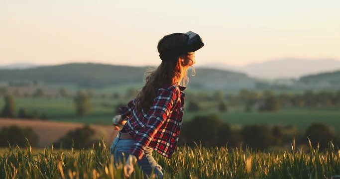 Woman Using Virtual Reality Glasses Outdoors. SLOW MOTION 4K. Young female playing in VR headset, touching virtual objects while standing in the field. Virtual reality world concept. 