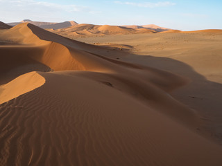 Fototapeta na wymiar Walking on natural curved ridge line through wind blow pattern of rusty red sand dune with soft shadow on vast desert landscape horizon background, Sossus, Namib desert