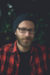 Happy hipster sitting outside with plants in the background.