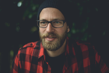 Happy hipster sitting outside with plants in the background.