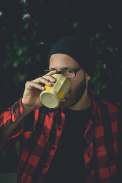 Happy Hipster Sipping A Cup Of Coffee On His Porch In The Morning In A Natural Setting.