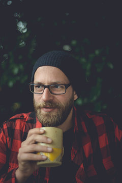 Happy Hipster Sipping A Cup Of Coffee On His Porch In The Morning In A Natural Setting.