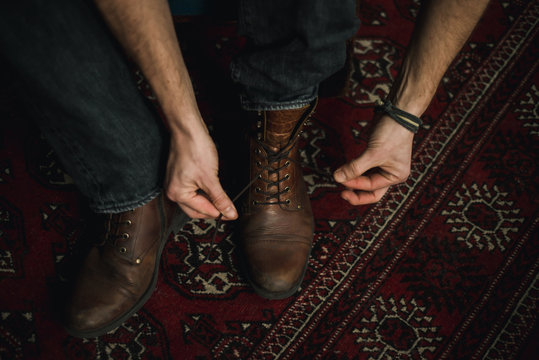 Close-up Perspective. Man Is Inside Tying Up The Laces Of His Brown Leather Boots Getting Ready To Go Out. 