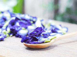 Wooden spoon with blue butterfly pea flowers on wooden table.