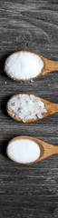 Different types of salt. Top view on black in wood spoons. Copy space.