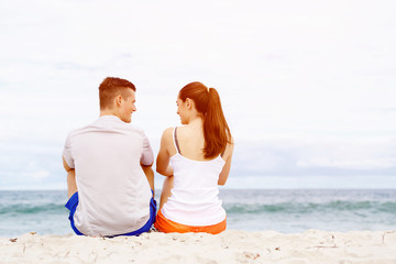 Fototapeta na wymiar Young couple looking at each other while sitting on beach