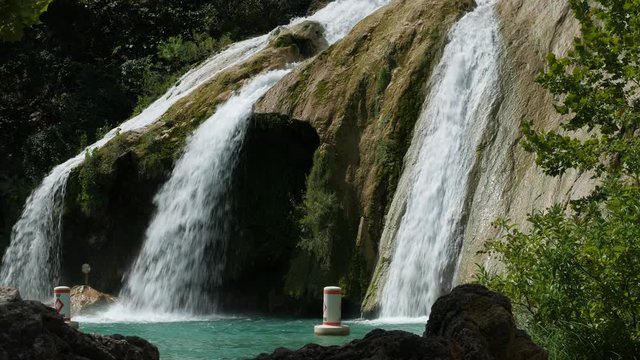 Steady close up shot, side view angle of Turner Falls framed by tree leaves and big boulders The 77-foot Turner Falls is one of the most popular summer destinations in Davis, Oklahoma