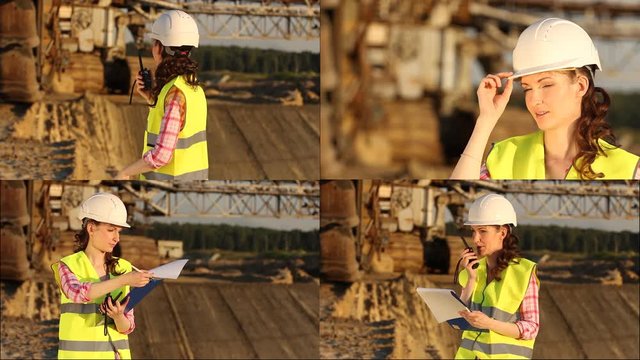 Pretty woman in helmet discusses something by walkie talkie with huge excavator on background