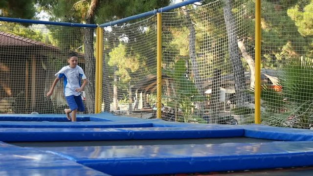 happy little boy  in shirts and a T-shirt actively spends his leisure actively pouncing from the trampoline to the trampoline on the playground in the park in the open air, slow motion