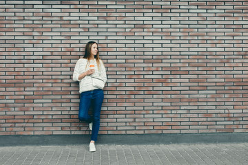Fototapeta na wymiar Trendy Girl Standing At The Brick Wall Background With Coffee