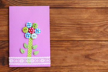 Happy Mother's day or birthday greeting card with flower isolated on a wood background with empty place for text. Card made with the use of wooden buttons, lace, paper, plastic leaves, glue, scissors