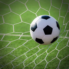 Naklejka na ściany i meble Soccer football in Goal net with green grass field.