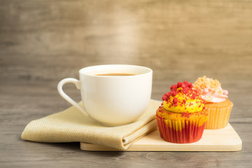 Side view of black coffee cup with red velvet and strawberry cupcakes on wooden plate on wooden table top