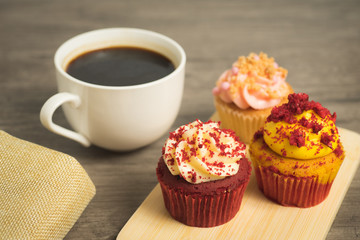 Black coffee cup with red velvet and strawberry cupcakes on wooden plate on wooden table top