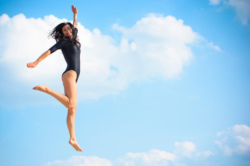 A young woman in tights is engaged in gymnastics and jumps, drains, leads herself into a good shape. Pleasure from training. Girl jumping against the sky