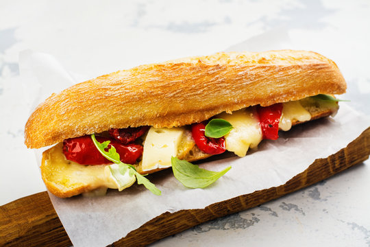Baked baguette sandwich with dried tomatoes, brie cheese and rocket salad