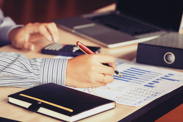 Businessman hand pointing to graph summary report and calculate finance with laptop searching data information on desk at office room.