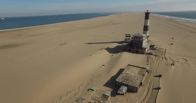 Aerial drone footage of desert sand peninsula, old lighthouse and power station building on ocean seals beach, Walvis Bay lagoon view with sea background and ships at Namibia's Atlantic west coast