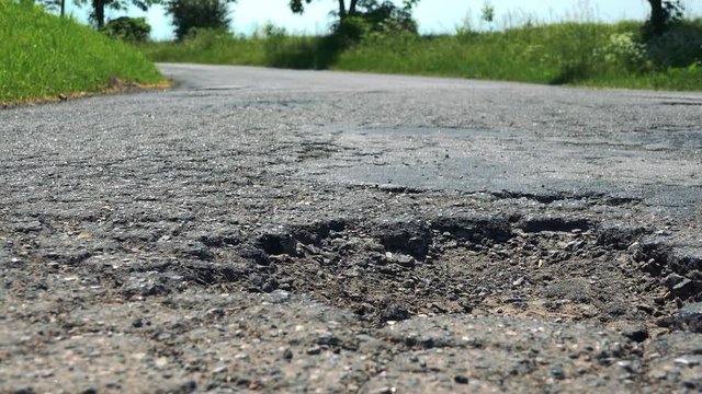 Detail of hole in asphalt in sunny day, road with nature in the background 
