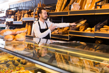 Male shop assistant demonstrating delicious loaves of bread in bakery